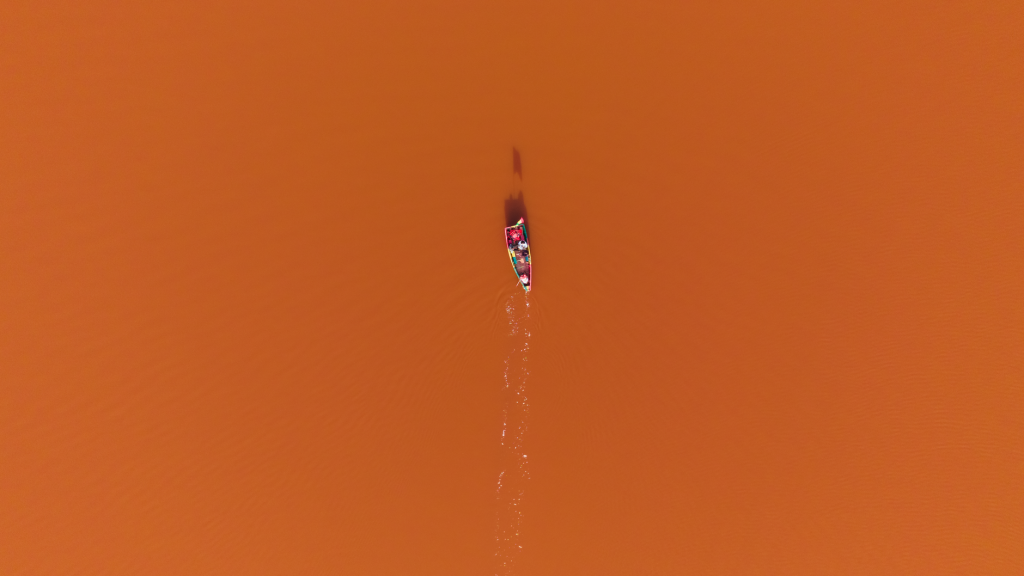 Drone shot of a colorful canoe navigating the orange waters of Lake Retba, Senegal.