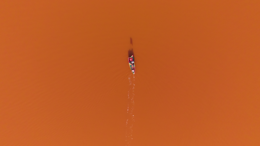 Drone shot of a colorful canoe navigating the orange waters of Lake Retba, Senegal.