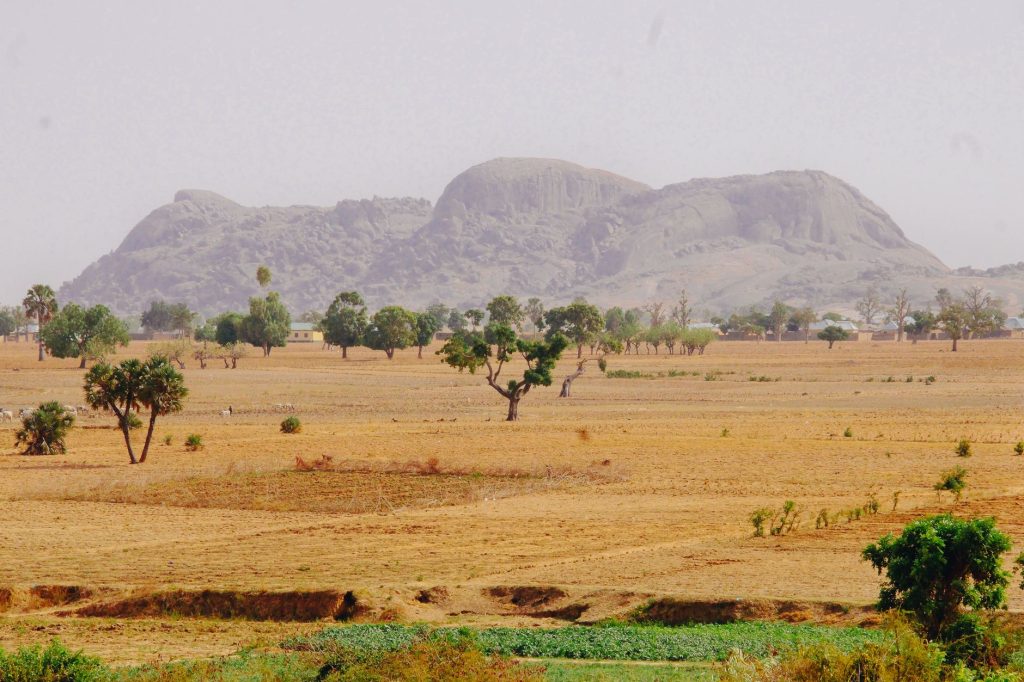 Expansive view of Nigerian savannah with distant hills and trees under a clear sky.