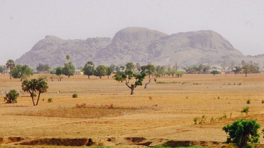 Expansive view of Nigerian savannah with distant hills and trees under a clear sky.