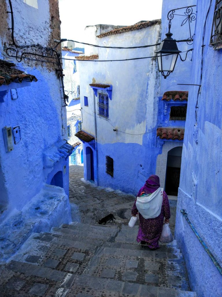 Habitante marchant dans un escalier bleu de la médina de Chefchaouen